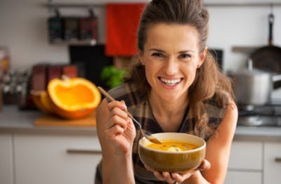 woman leaning on counter smiling, holding bowl of food you can eat with dysphagia