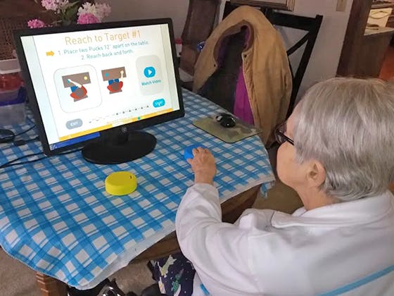 senior stroke survivor using FitMi at home with large computer screen
