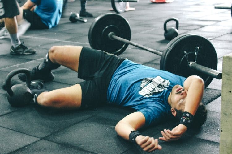 man lying on the floor of gym exhausted because he started weight lifting too soon after brain injury