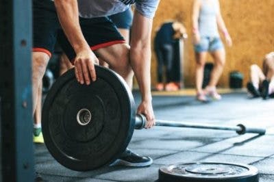 man sliding weights on to barbell in gym