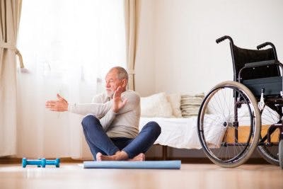 stroke patient doing stretches at home with wheelchair off to the side