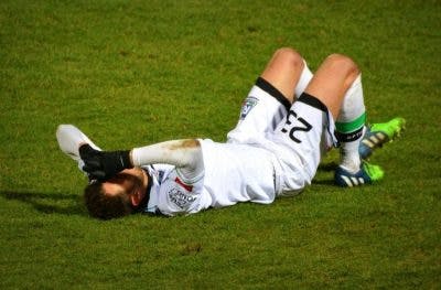 soccer player lying on grass holding his head because he has a concussion