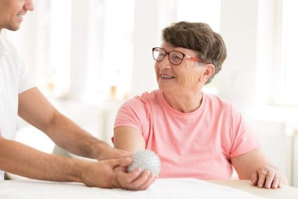 physiotherapist helping survivor with hand spasticity treatment by stretching hand with ball