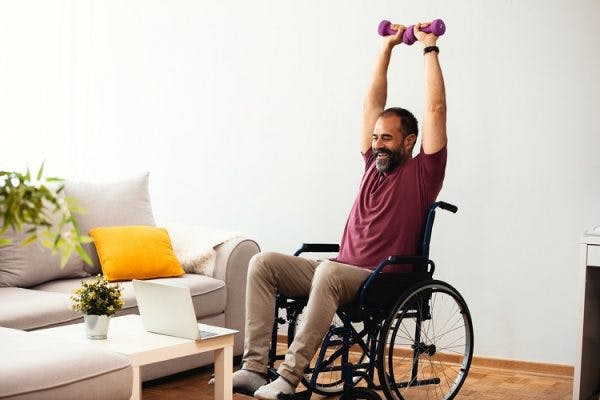 man in wheelchair happily practicing upper extremity exercises for spinal cord injury at home