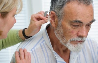 Doctor inserting hearing aid in patient's ear to help with hearing loss after head injury