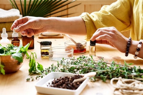 Woman preparing tinctures of natural remedies for post concussion syndrome at table full of herbs and essential oils