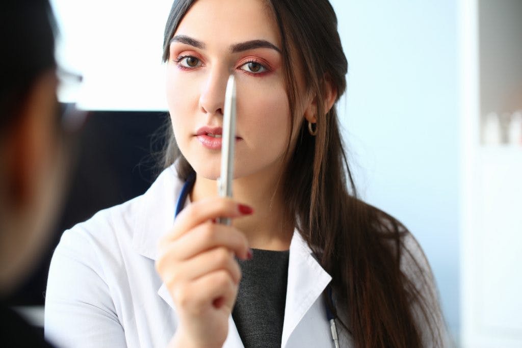 doctor holding pen in front of patient's eyes, showing patient how to do pencil pushups as eye exercises for concussion