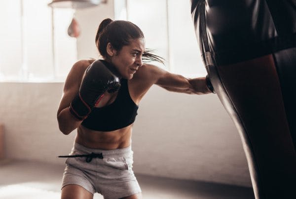 female with boxing gloves punching a bag to let out aggressive behavior after brain injury