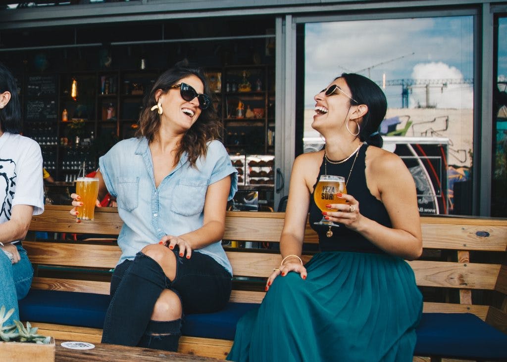 two friends laughing and holding drinks and improving their social skills after brain injury