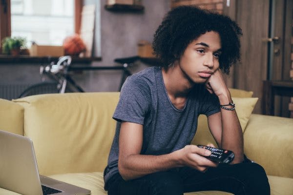 teenager sitting on couch bored and holding remote, struggling with lack of motivation after brain injury