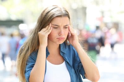 girl rubbing her head in a crowded street, looking worried because she is about to have a seizure after head injury