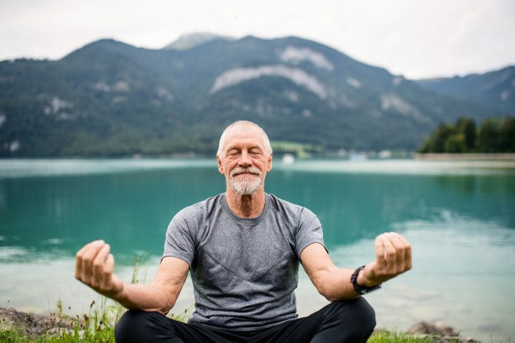 senior man pensioner sitting by lake, practicing mindfulness after brain injury.