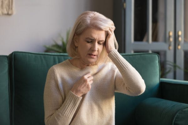 woman sitting on couch closing eyes experiencing nausea and vomiting after head injury