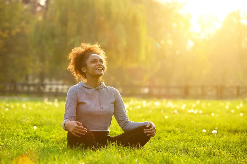 Happy young woman smiling and sitting on grass, practicing mindfulness after brain injury