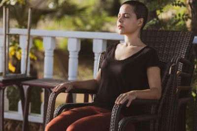 woman closing eyes and sitting in chair on porch, learning mindfulness after brain injury