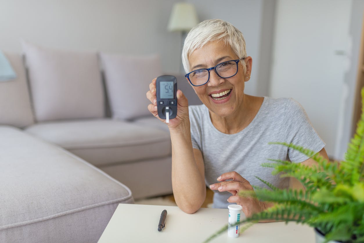 woman smiling and checking blood sugar level at home