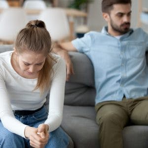 girlfriend sitting on couch crying while boyfriend sits back ignoring her because he has lack of empathy after brain injury