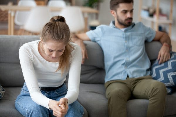 girlfriend sitting on couch crying while boyfriend sits back ignoring her because he has lack of empathy after brain injury