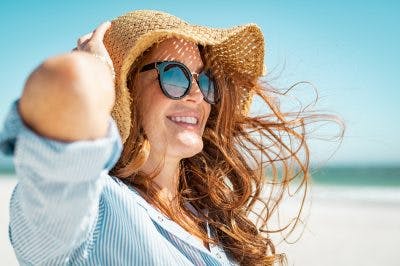 woman with sun hat and summer blouse smiling on beach