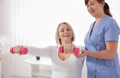 stroke patient holding up dumbbells with help of a physical therapist