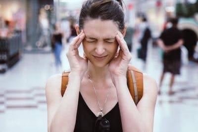 woman in mall closing her eyes and rubbing her head because she is having a sensory overload, a common symptom of both TBI and autism