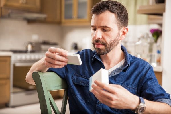 man sitting at kitchen table reading label of Adderall for TBI