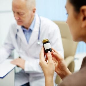 woman reading label of bottle of aricept for brain injury while doctor writes instructions in the background