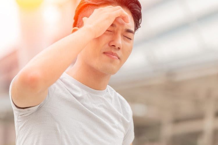 Man holding head squinting in bright sunlight because he has light sensitivity after brain injury