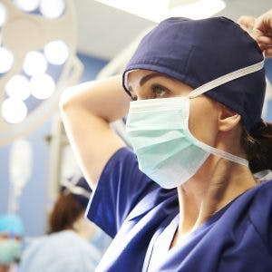 Side view of young female surgeon tying her surgical mask, discussing the types of surgery for head injury with her colleagues