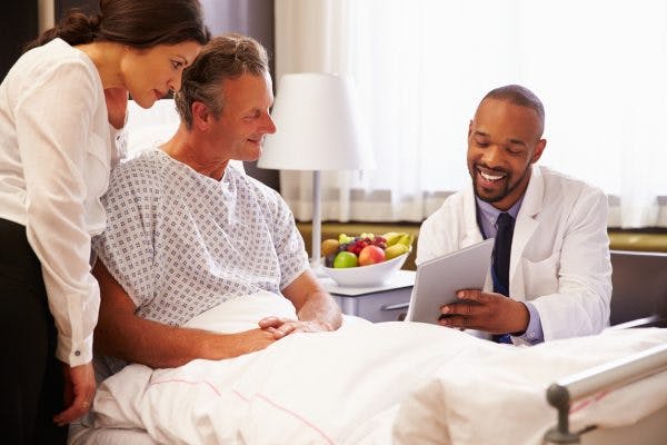 Doctor talking to male patient and wife in hospital bed about what to expect after brain injury