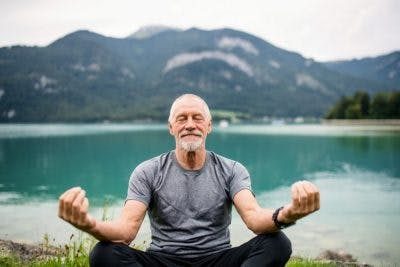 healthy senior man meditating in front of mountain lake