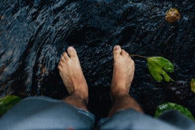 top view of man's bare feet standing in shallow stream