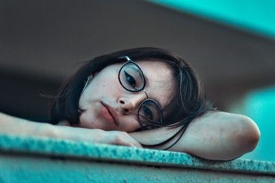 girl with glasses leaning head on table, looking bored and detached because she has flat affect after brain injury