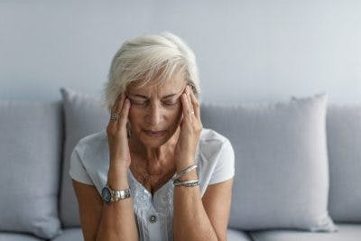 senior woman sitting on couch rubbing temples and closing her eyes