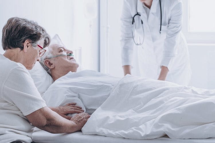 Frau sitzt neben Krankenhausbett mit Ehemann im Koma nach Schlaganfall