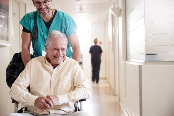Man being pushed in wheelchair smiling because he is leaving the hospital after stroke