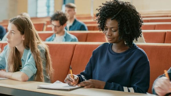 College student smiling and writing in her notebook during lecture, learning how to accommodate traumatic brain injury in the classroom