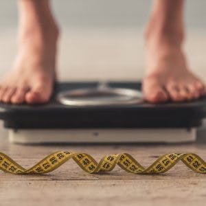 Cropped image of woman feet standing on weigh scales to measure her weight gain after brain injury. A tape measure lies on the floor in the foreground