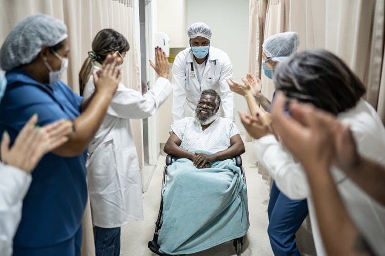 man in wheelchair leaving the hospital after a stroke while a crowd of nurses cheers for him
