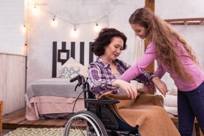 young daughter wrapping heated blanket around her mother's legs because she has cold feet after spinal cord injury