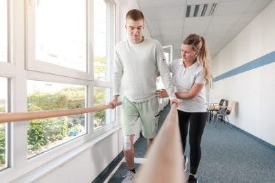 young man using parallel bars in rehab hospital, learning to walk because of stem cell therapy for brain injury