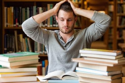 college student surrounded by books in library looking overwhelmed