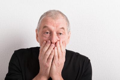 old man covering his mouth over his hands because he has just said something rude