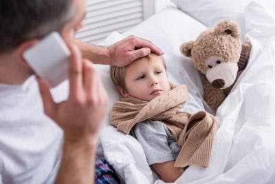 child with cerebral palsy lies in bed sick with flu while father calls the doctor