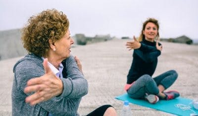 elderly stroke patient and daughter stretching on yoga mats on beach