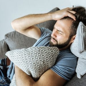 man laying on couch clutching pillow and pulling his hair because he has agitation after traumatic brain injury