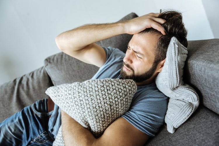 man laying on couch clutching pillow and pulling his hair because he has agitation after traumatic brain injury