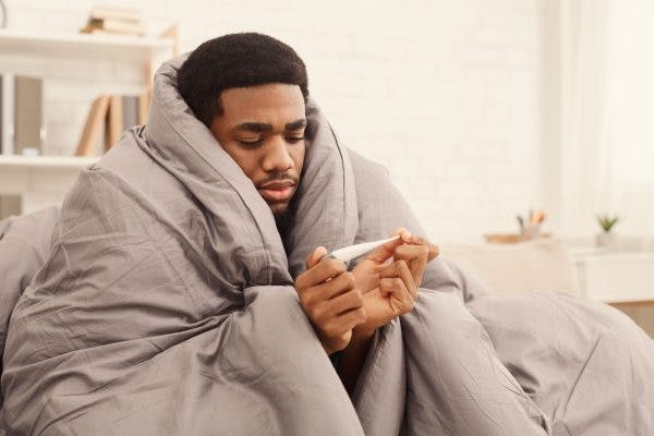 man wrapped in heavy blankets reading his temperature because he is feeling cold after head injury