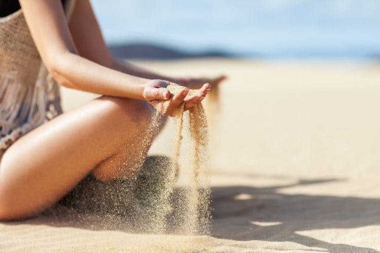 Woman practicing sensory activities for TBI by letting sand run through her hands while sitting at the beach, the camera is focused on her hands