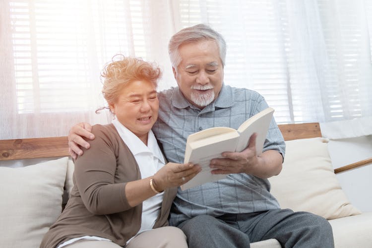 elderly married couple reading a stroke book together on a sofa
